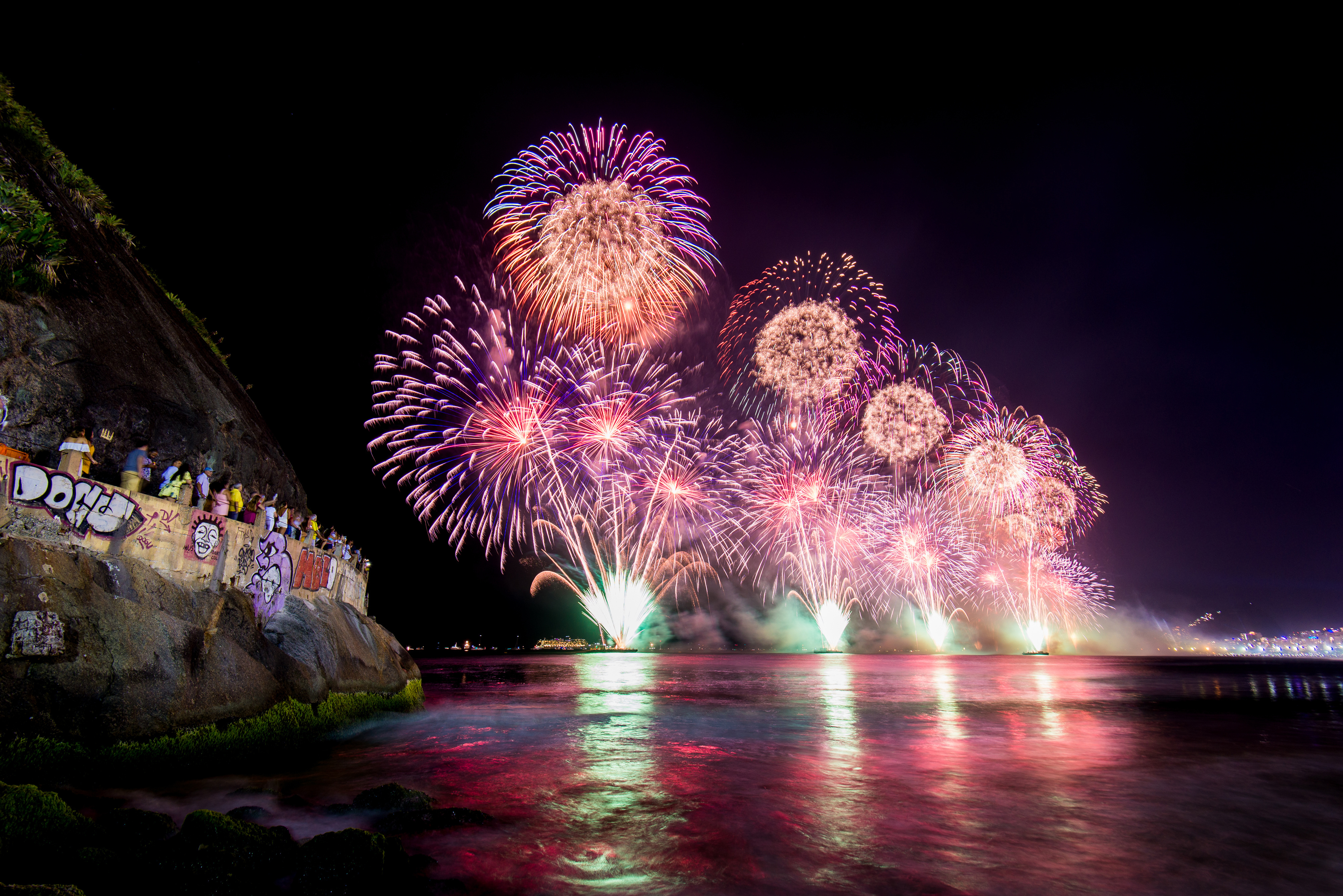 Fireworks over the water, viewed from a graffiti-covered cliffside