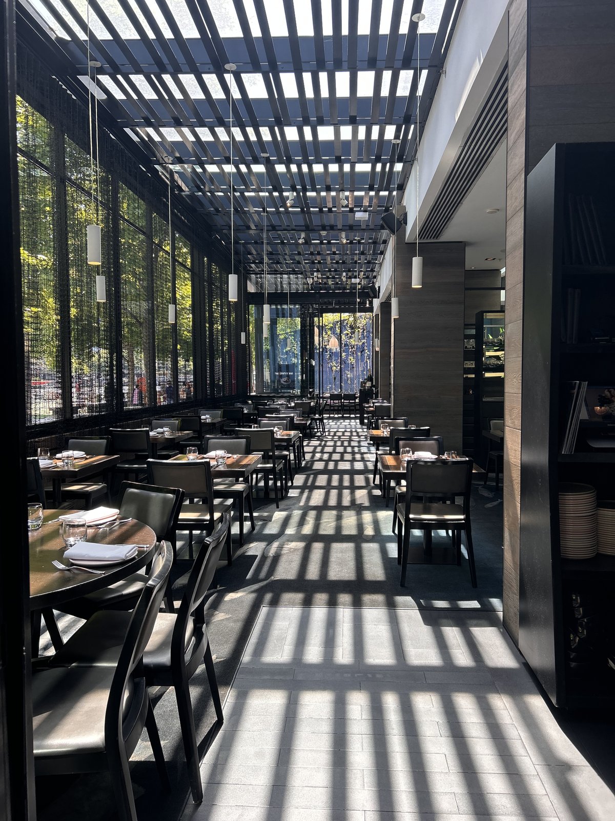 Sunlit restaurant terrace with dappled shadows from a slatted pergola roof, Melbourne